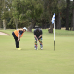 Golfer lining up on the green ready to putt while the Caddie is standing behind giving instructions